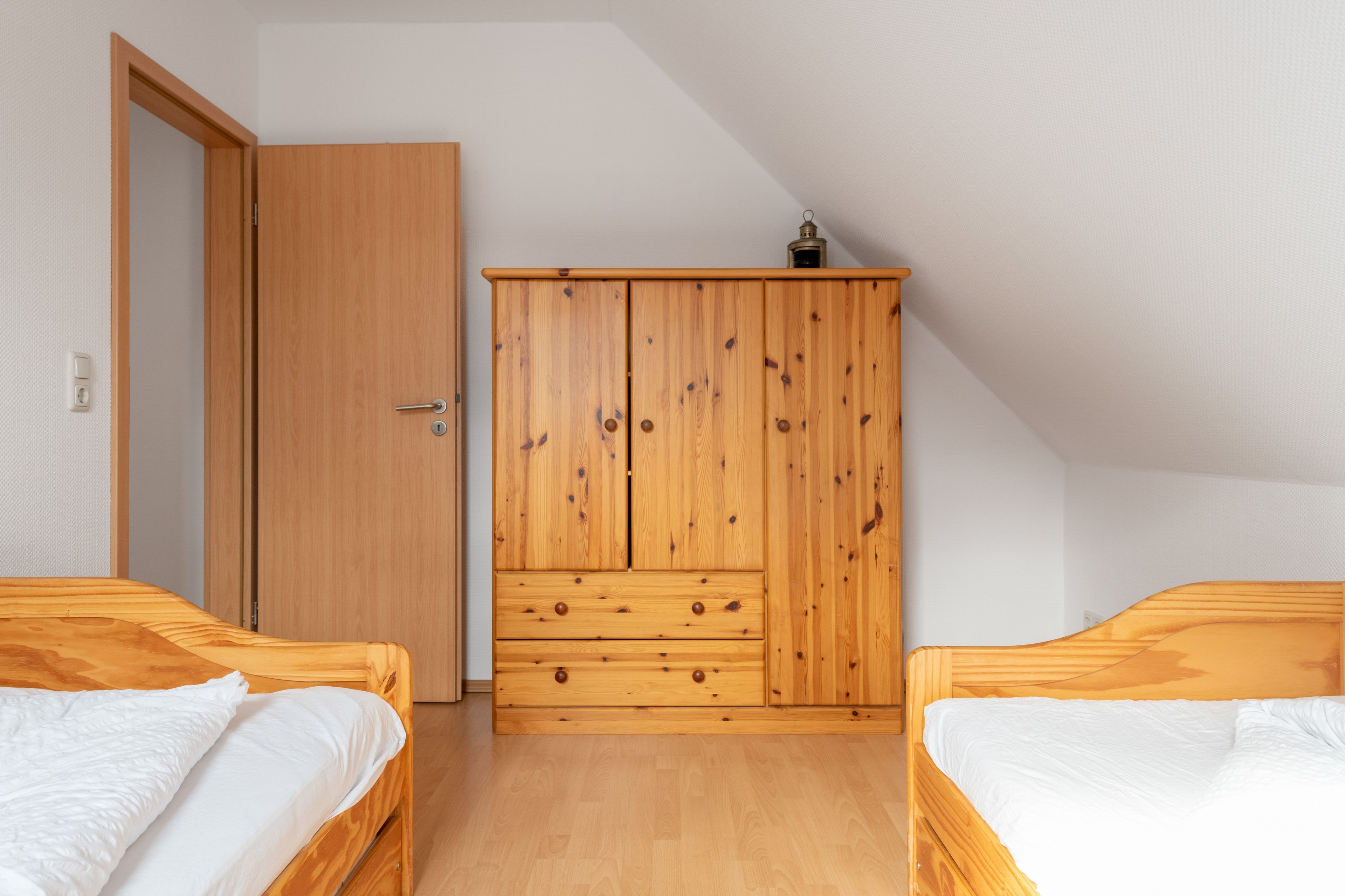 A bedroom with two wooden beds, a wooden wardrobe, and a door.