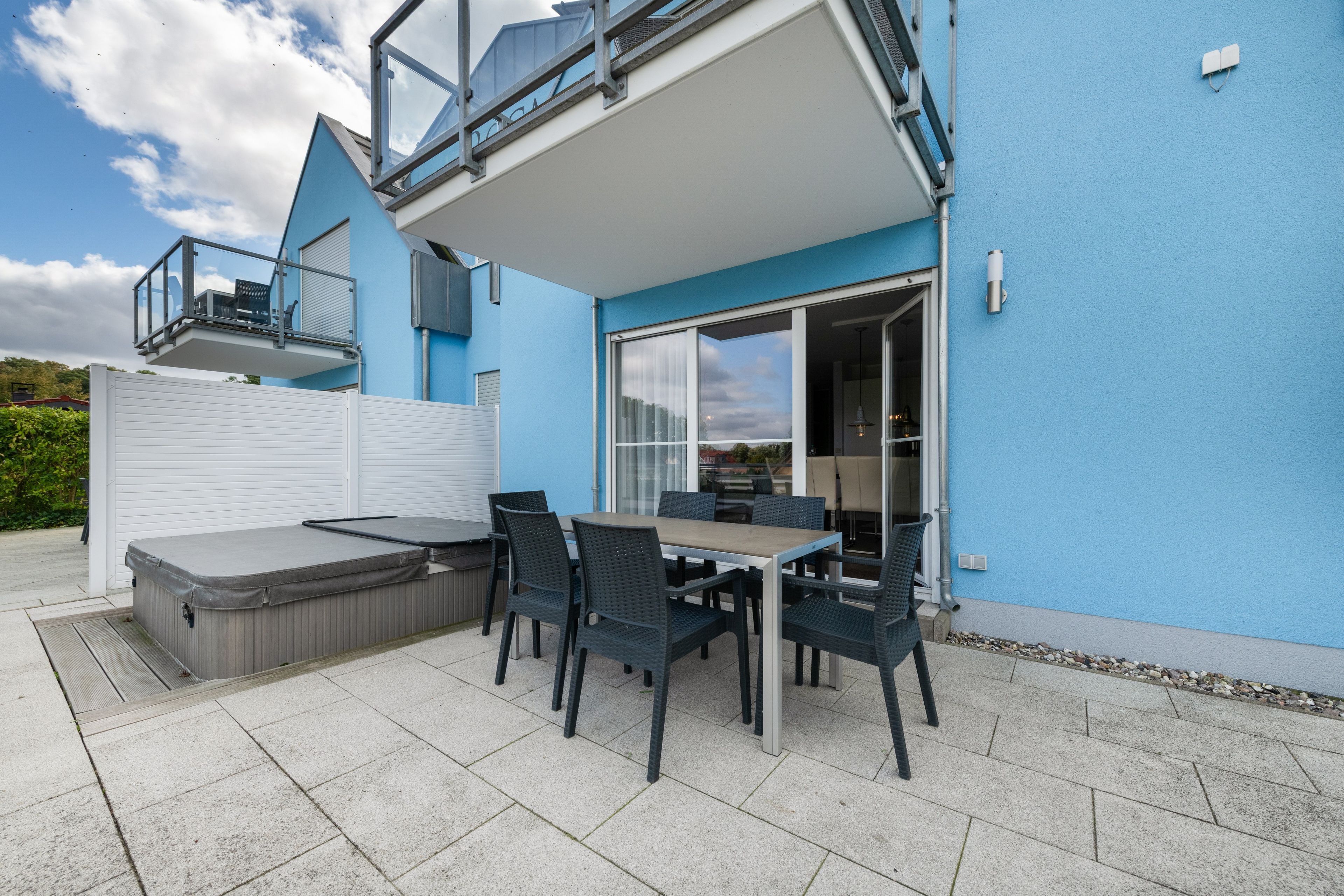 A modern outdoor patio with a hot tub, dining table, and chairs.