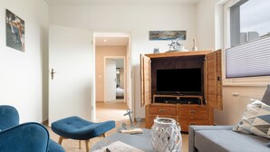 Un salon moderne avec un téléviseur à écran plat, un meuble en bois et un coin salon confortable.