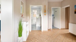 Um corredor com porta branca, espelho, planta e cabideiro.