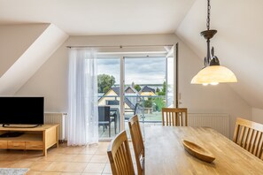 En matplats med ett bord, stolar, en tv och utsikt över husen genom ett stort fönster.