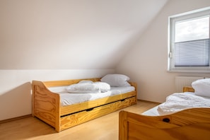 Eine kleine Einzimmerwohnung mit schrägverdachter Decke, einem Holzbett und einem Fenster mit Jalousien.