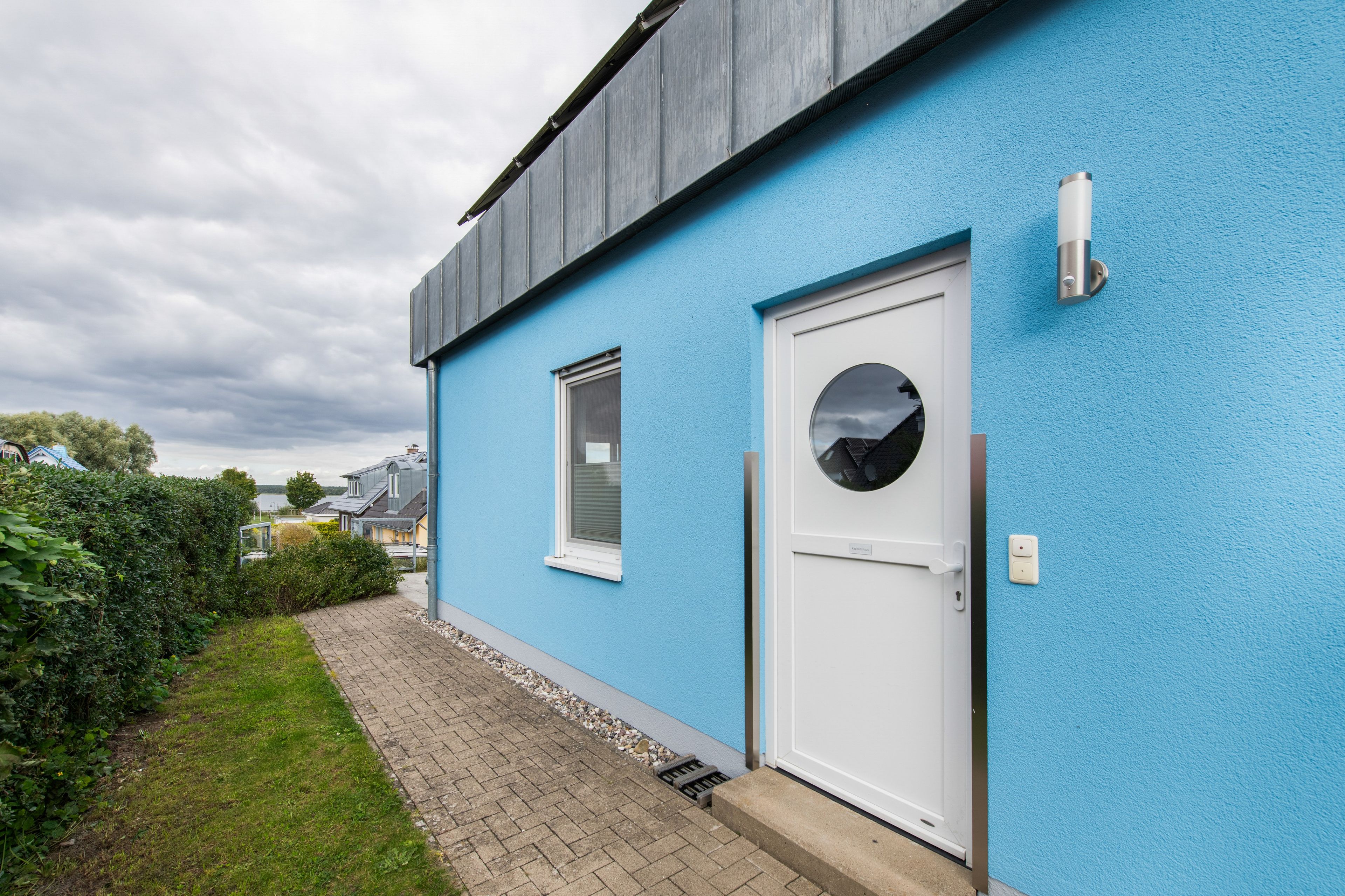 Ein modernes Haus mit blauer Fassade, einer weißen Tür und einem kleinen Fenster.