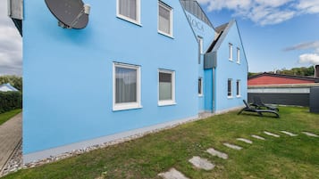 Ein blaues Gebäude mit Satellitenschüssel, einer Tür und einem kleinen Garten mit trittfesten Steinen.