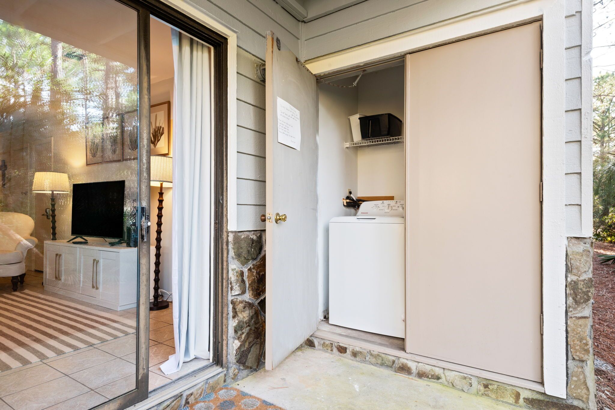 A room with a glass door leading to a stone wall, a white cabinet, and a television on a cabinet.