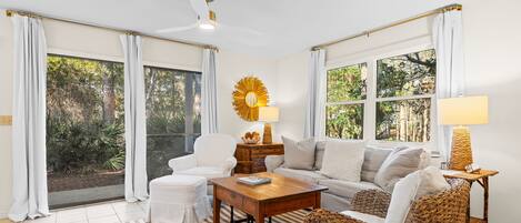 Une pièce avec un ventilateur de plafond, un canapé, une table basse, un fauteuil en osier et une lampe.