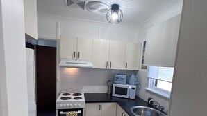 A compact kitchen with white cabinets, a stove, a microwave, and a sink.