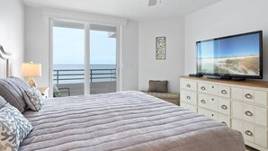 Una camera da letto con un letto, una televisione, una ventola a soffitto, un comò e un balcone vista oceano.