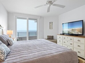 Ein Schlafzimmer mit Bett, Fernseher, Deckenventilator, Kommode und einem Balkon mit Meerblick.
