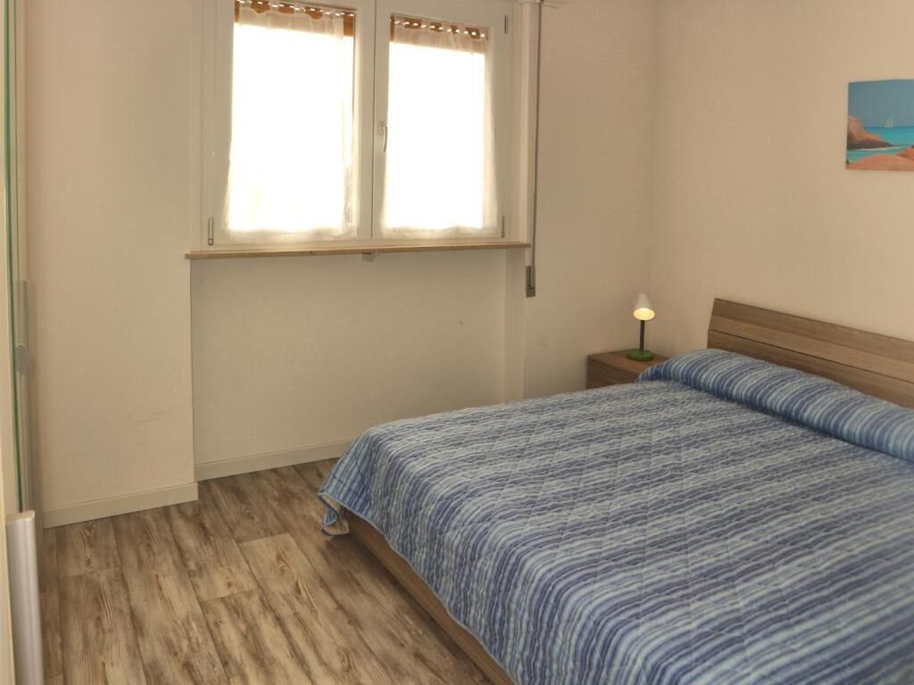 Ein Schlafzimmer mit einem Bett, einem Nachttisch, einer Lampe und einem Fenster.