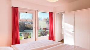 Ein Schlafzimmer mit einem Bett, einem Fenster mit roten Vorhängen und einer Tür, die in einen anderen Raum führt.