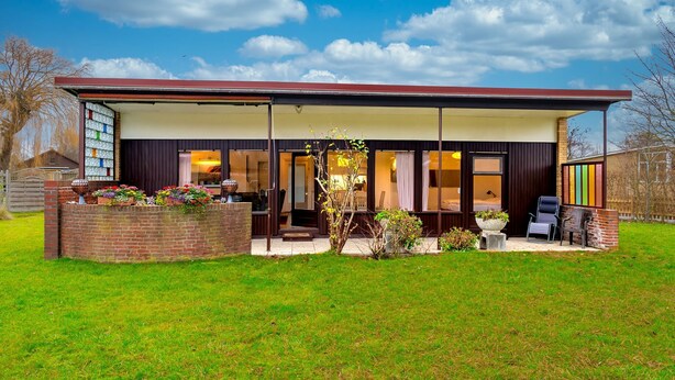 Ein modernes Haus mit einer überdachten Terrasse, einer Ziegelmauer im Garten und einem Rasen.