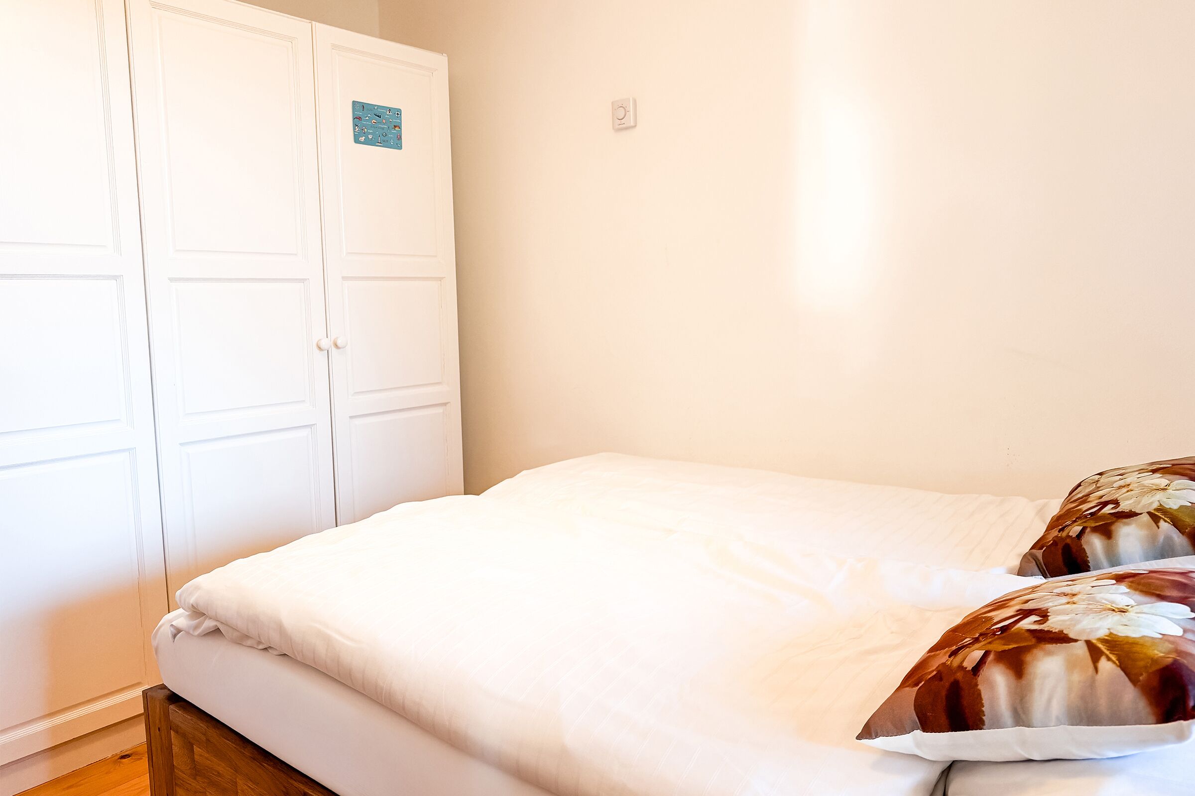 A bedroom with a white bed, wooden headboard, and a white wardrobe.