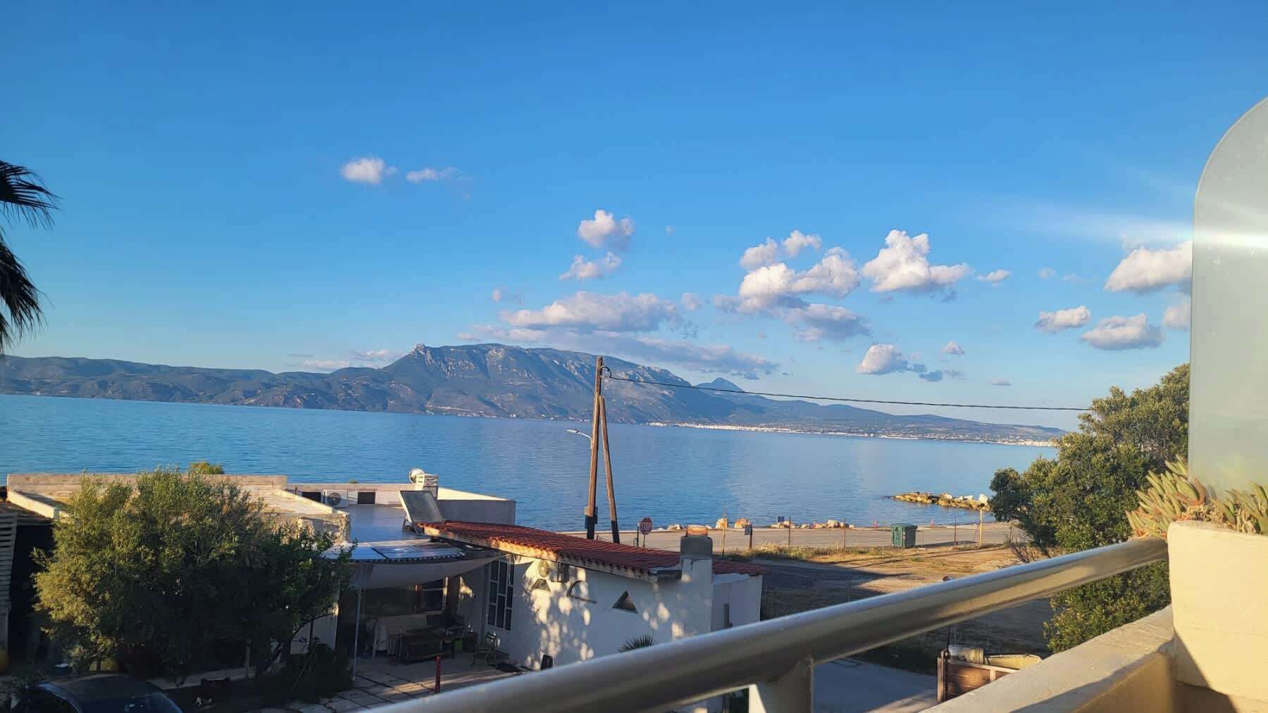 The balcony table and chairs with the Gulf of Corinth spread out directly in front — this is where most mornings will start and most evenings will end, with a view that earns the studio its place on the waterfront.