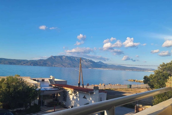 The balcony table and chairs with the Gulf of Corinth spread out directly in front — this is where most mornings will start and most evenings will end, with a view that earns the studio its place on the waterfront.
