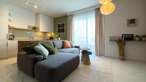 Ein modernes Wohnzimmer mit einem grauen Sofa, einem kleinen runden Tisch und einer Küche im Hintergrund.