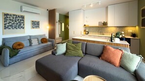 Ein modernes Wohnzimmer mit einem grauen Ecksofa, einer kleinen Küchenzeile und einer grünen Akzentwand.