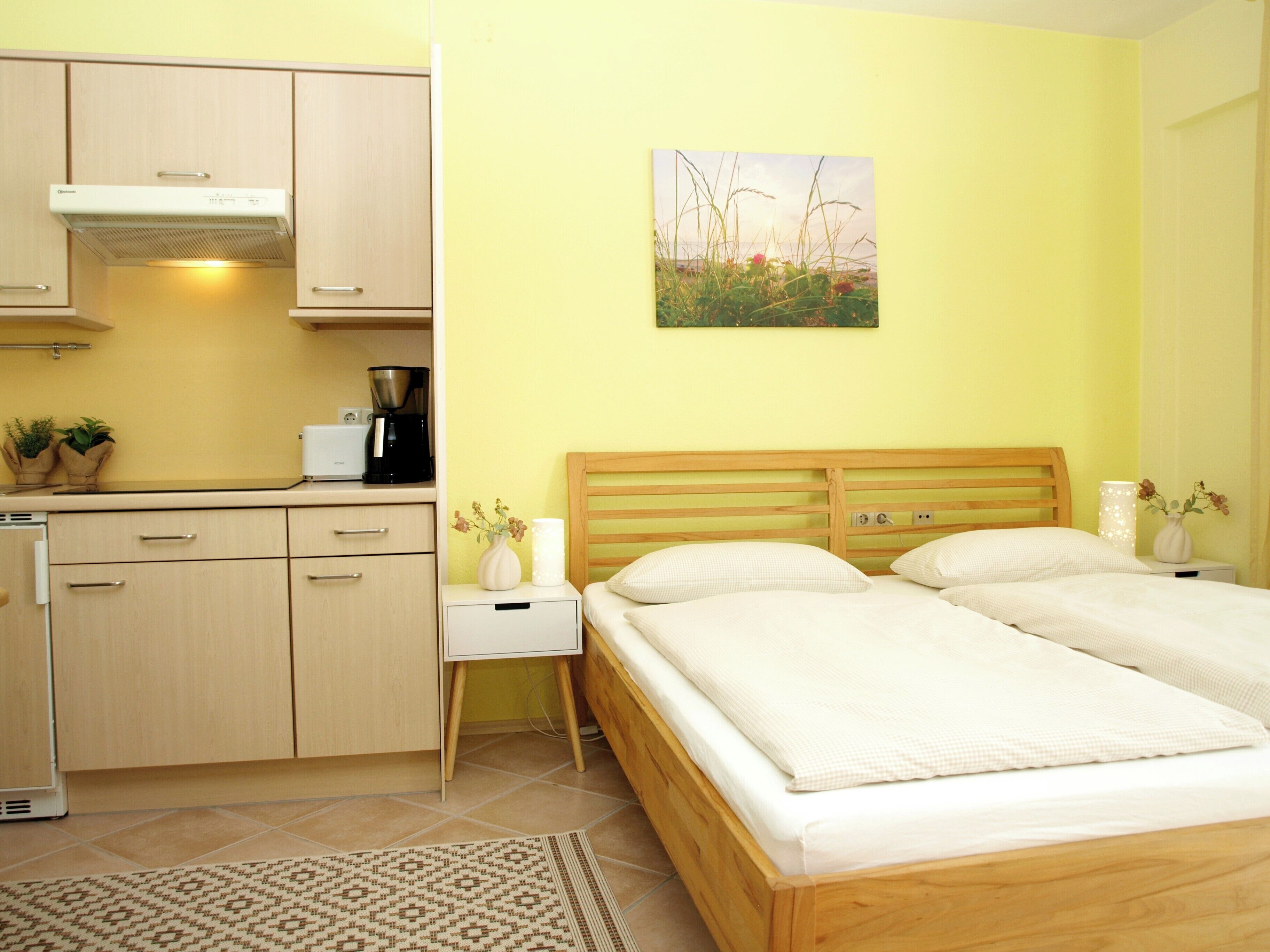 A bedroom with a bed, bedside table, and a small kitchenette.