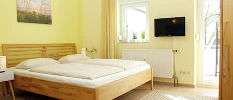 A bedroom with a bed, bedside table, lamp, TV, window, and a view of the outside.