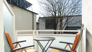 Un balcon avec deux chaises et une petite table, donnant sur un immeuble et un arbre.