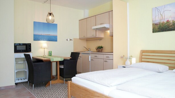 Une chambre d’hôtel compacte comprenant un lit, une petite kitchenette, un coin repas avec une table et des chaises, et une vue sur la mer.