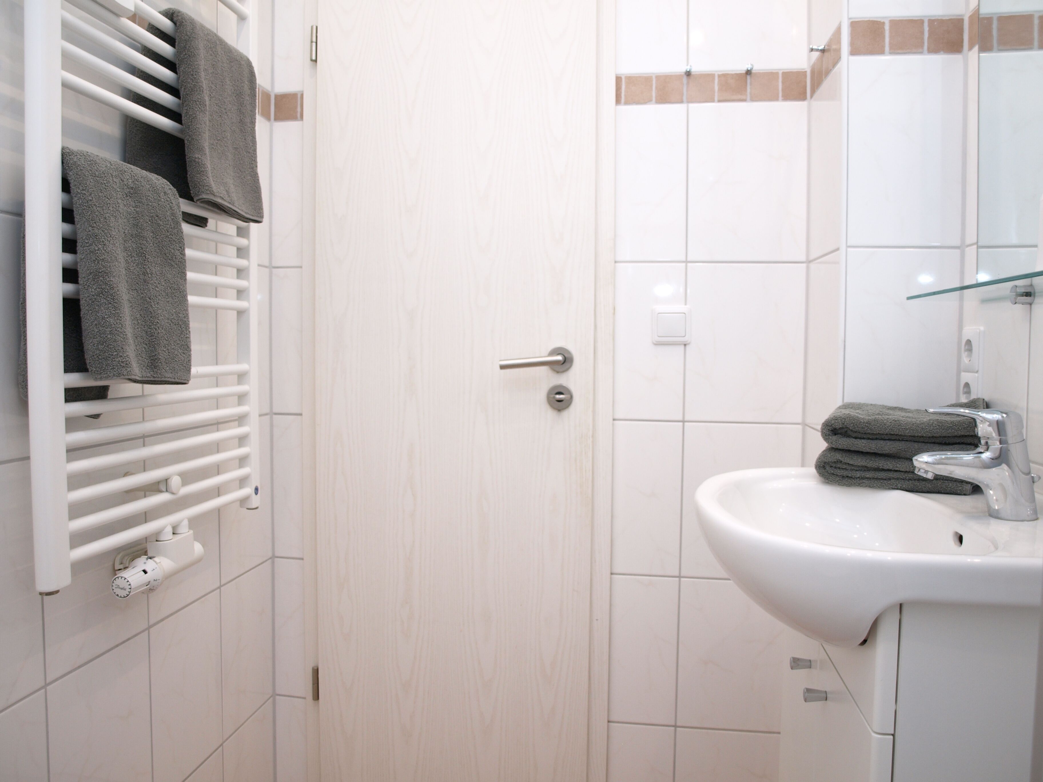 Une salle de bain avec un lavabo blanc, un miroir et un porte-serviettes avec des serviettes.