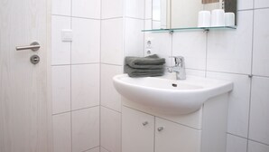 Une salle de bain avec un lavabo blanc, une étagère en verre au-dessus et une serviette accrochée au mur.
