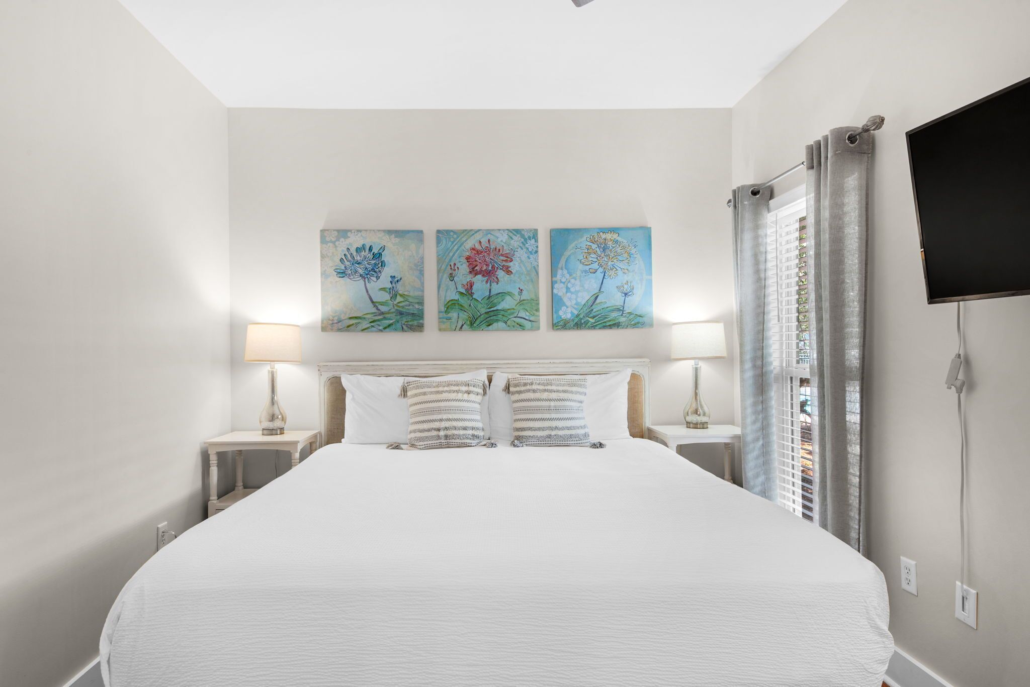 Ein Hotelzimmer mit einem großen Bett, zwei Nachttischen, einem Flachbildfernseher und drei floralen Bildern an der Wand.