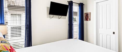 A bedroom with a bed, a TV mounted on the wall, a door, and blue curtains.