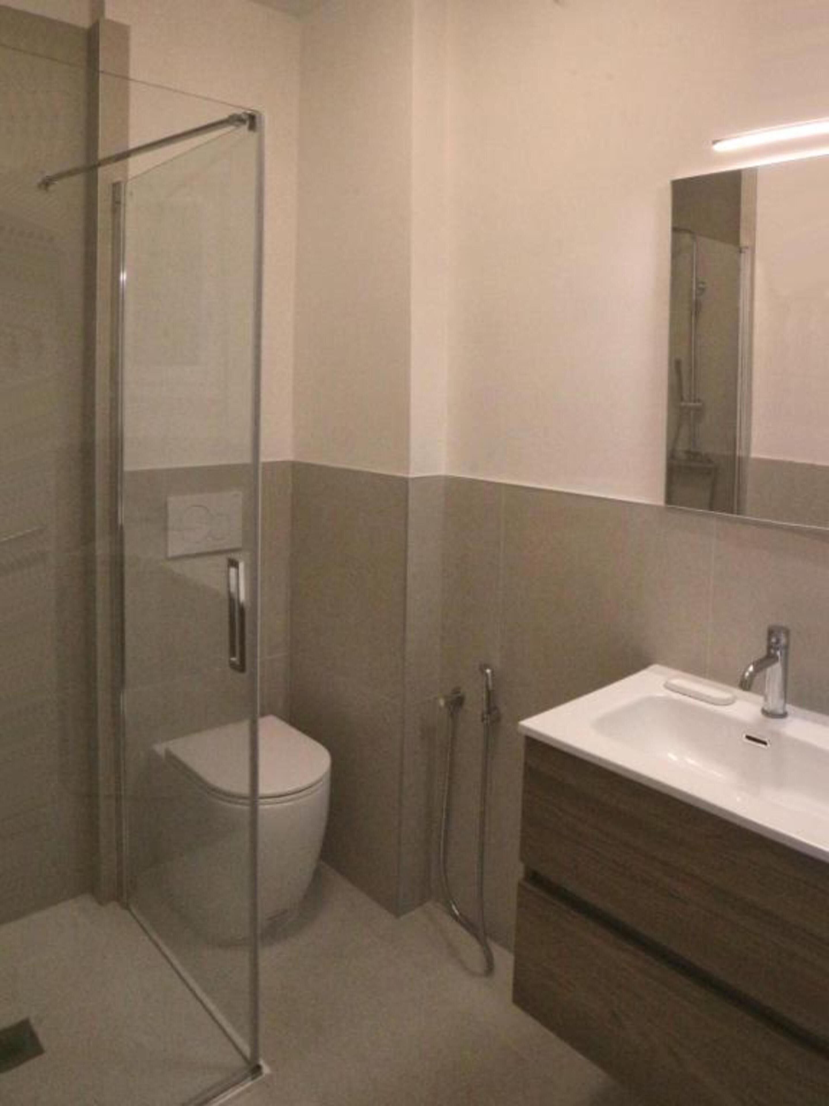 Une salle de bain avec une douche à parois de verre, des toilettes et un lavabo avec un miroir au-dessus.