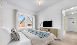 A bedroom with a bed, a TV, a wooden dresser, and a view of a brick building outside.