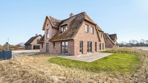 A modern house with a brick exterior, large windows, and a thatched roof. - Premium vacation home Große Halbe Düne in the dune park with terrace and sauna (List auf Sylt)