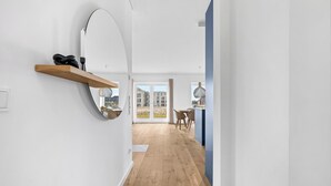 A modern interior with a wooden floor, a mirror, and a view through a glass door to an outdoor area. - Premium vacation home Große Halbe Düne in the dune park with terrace and sauna (List auf Sylt)
