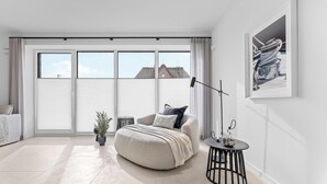 A modern bedroom with a large window, a sofa, a round table, and a potted plant. - Premium vacation home Halber Deich in the dune park with terrace and sauna (List auf Sylt)