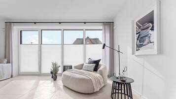 Een moderne slaapkamer met een groot raam, een bank, een ronde tafel en een potplant.