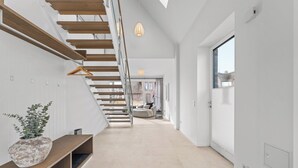 A modern interior with a staircase, a hanging light fixture, and a view through a large window. - Premium vacation home Halber Deich in the dune park with terrace and sauna (List auf Sylt)
