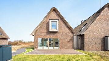 Een modern huis met een puntdak, een grote glazen deur en een houten terras.