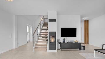 A modern living room with a staircase, a fireplace, a flat-screen TV, and a minimalist console table.