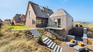 Une maison moderne avec un toit en pente, un balcon en verre et un escalier en pierre menant à l’entrée.