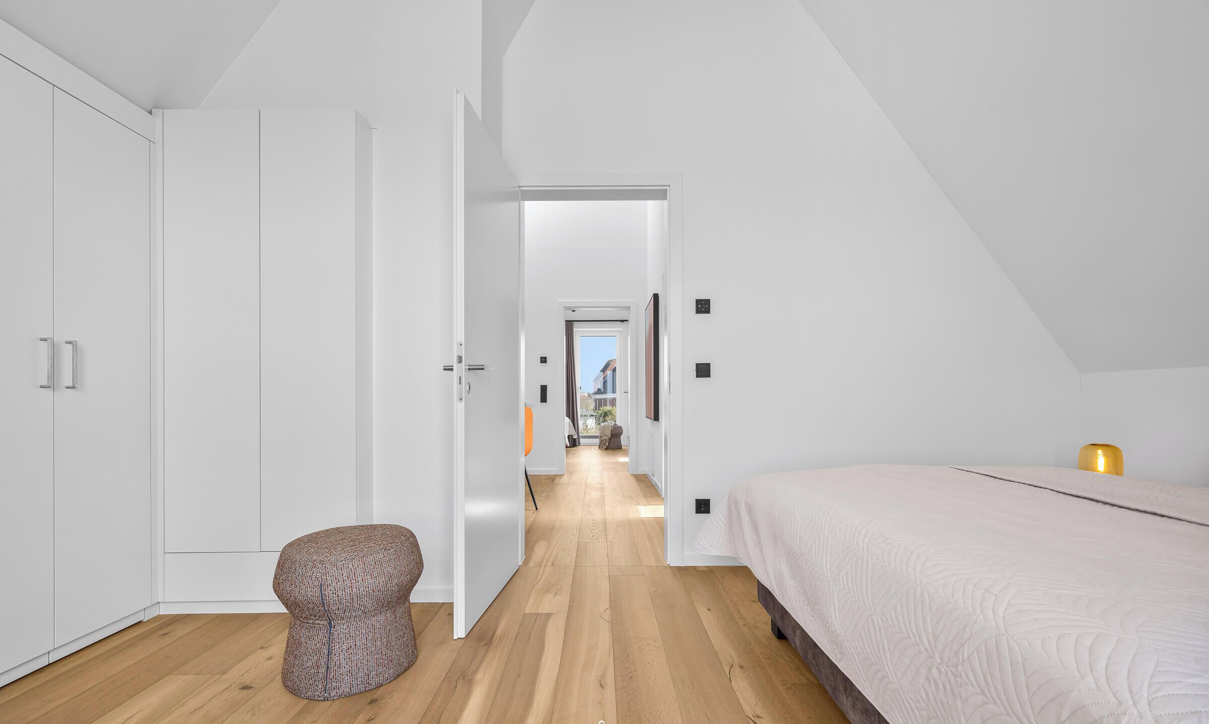 Une chambre à coucher moderne avec un lit, un petit tabouret et une armoire blanche.