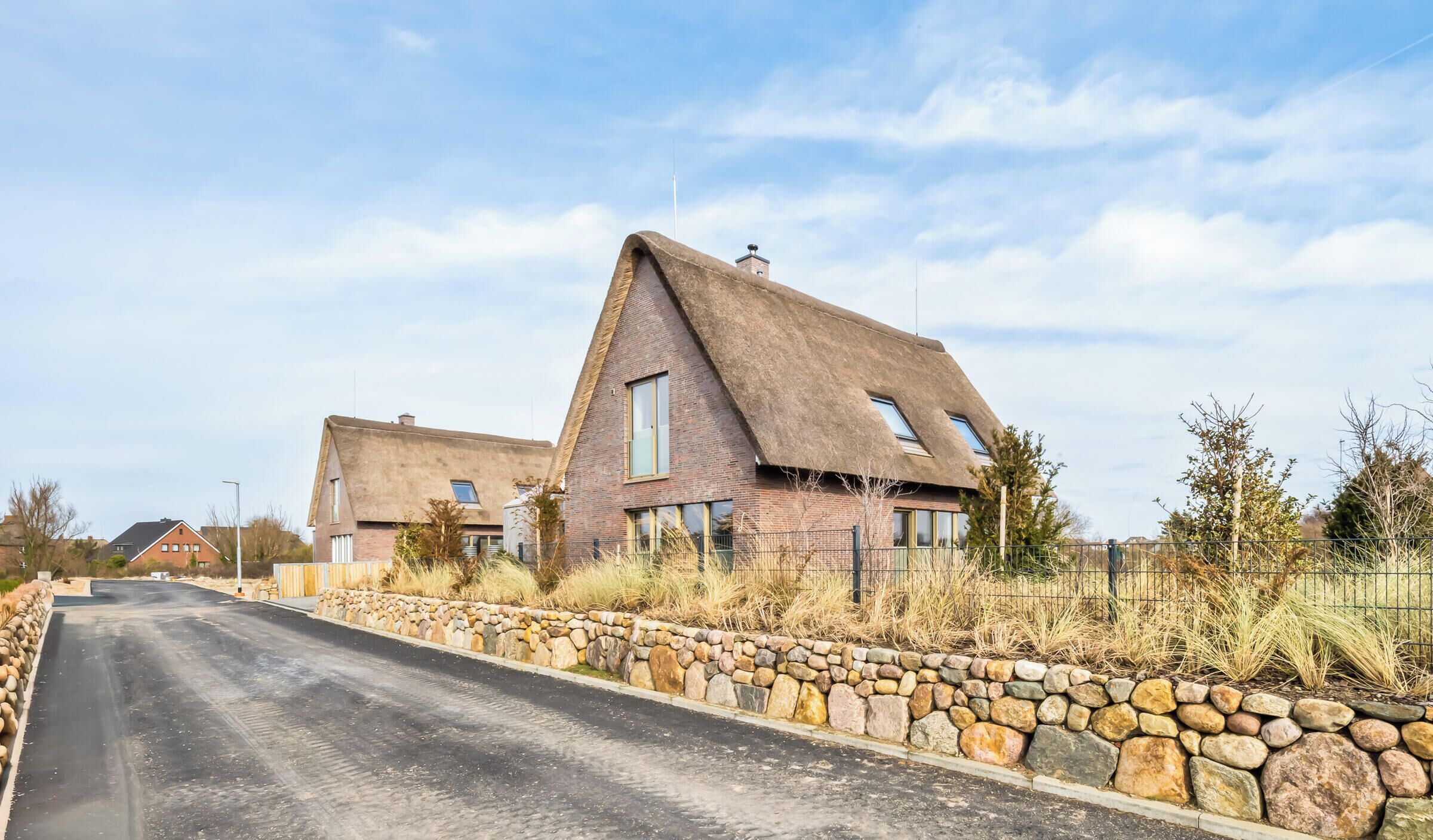 A rural road leading to a house with a thatched roof and stone walls.