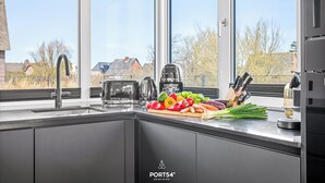 Une cuisine moderne dotée d’une grande fenêtre, d’appareils électroménagers en acier inoxydable et de légumes frais disposés sur le plan de travail.