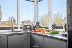 A modern kitchen with a large window, stainless steel appliances, and fresh vegetables on the counter. - Detached premium vacation home Villa Deich in the dune park with terrace and sauna (List auf Sylt)
