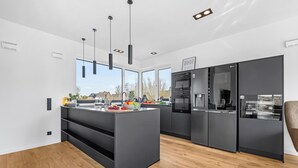 Une cuisine moderne dotée d’un îlot central, de meubles de rangement noirs et offrant une vue sur l’extérieur.