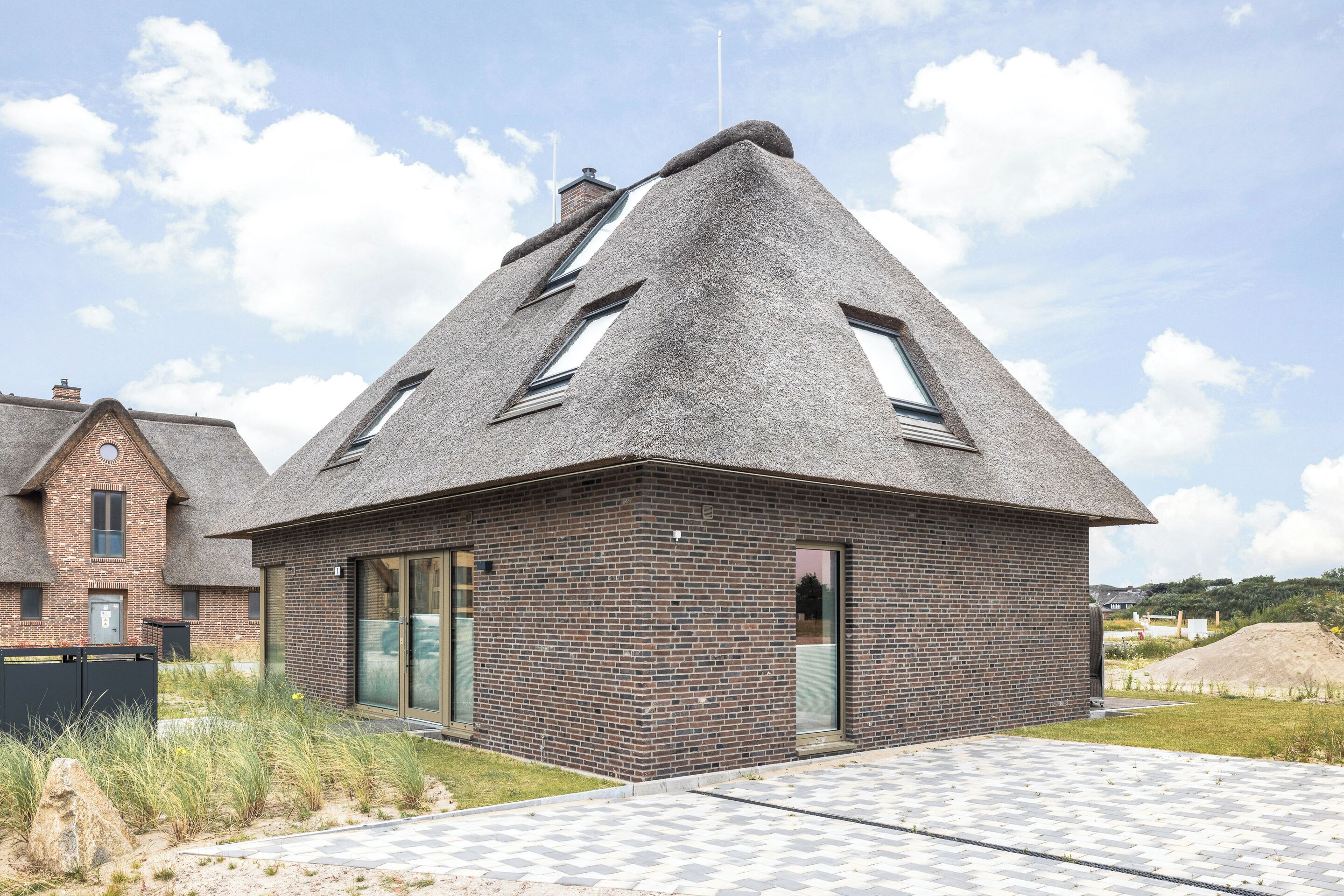 Ein modernes Haus mit einem steilen Satteldach, Backsteinwänden und großen Fenstern.