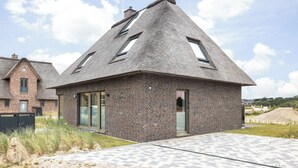 A modern house with a steeply pitched roof, brick walls, and large windows. - Premium vacation home Haus Deich in the dune park with terrace and sauna (List auf Sylt)