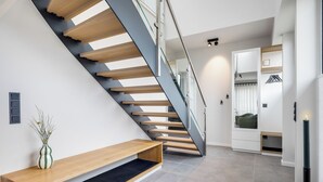 A modern staircase with wooden steps and glass railings, leading to a room with a built-in wardrobe and a bench. - Premium vacation home Haus Deich in the dune park with terrace and sauna (List auf Sylt)