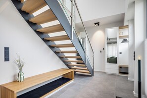 A modern staircase with wooden steps and glass railings, leading to a room with a built-in wardrobe and a bench. - Premium vacation home Haus Deich in the dune park with terrace and sauna (List auf Sylt)