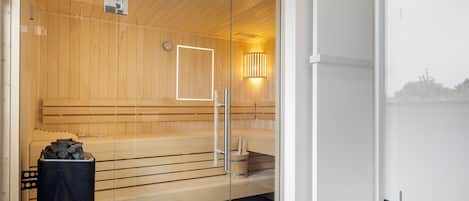 A sauna with wooden benches, a glass door, and a wall-mounted light fixture.