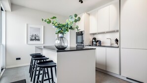 A modern kitchen with a central island, bar stools, a coffee machine, and a framed picture on the wall. - Premium vacation home Haus Deich in the dune park with terrace and sauna (List auf Sylt)